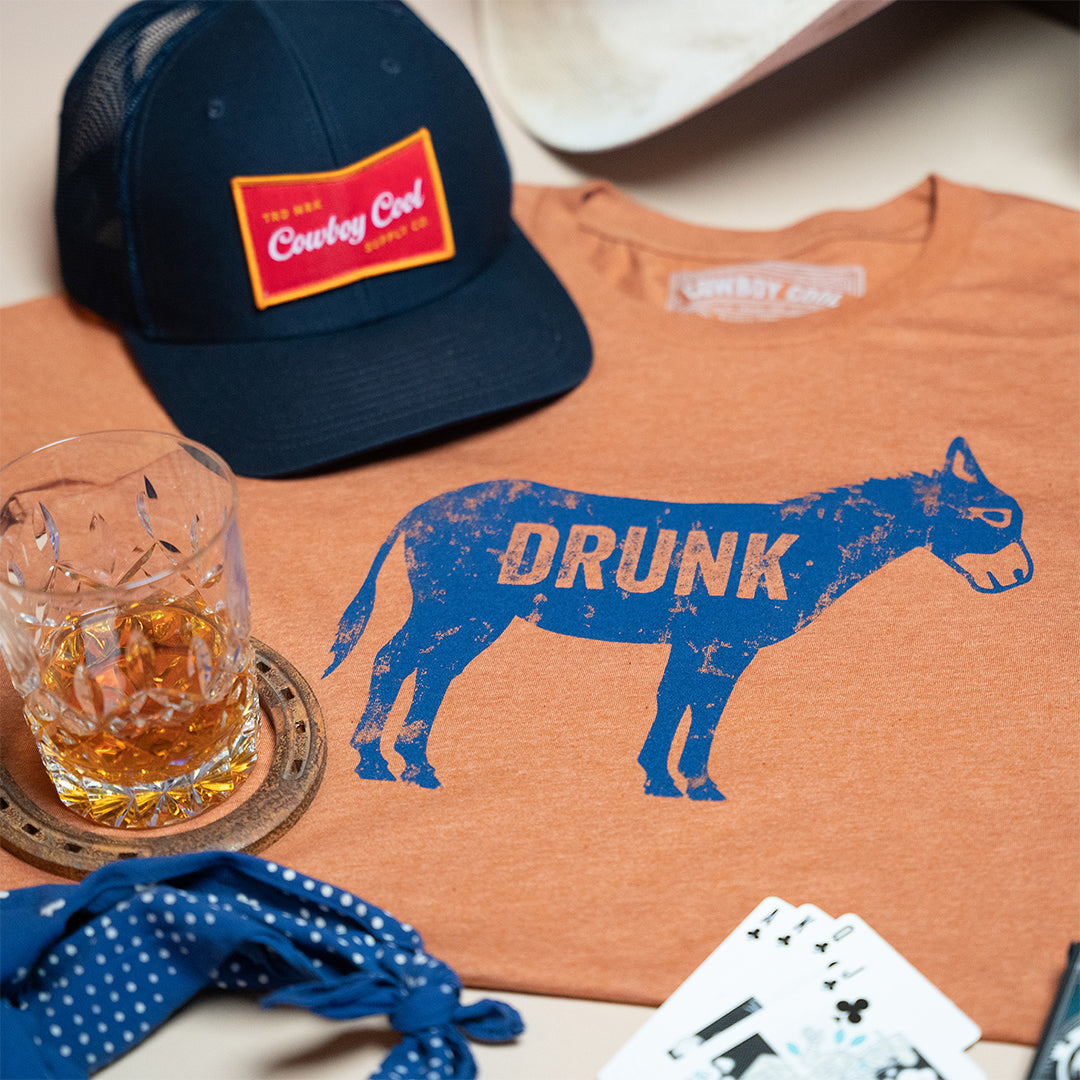Cowboy Cool Drunk Ass collection showing a t-shirt, hat a deck of cards.