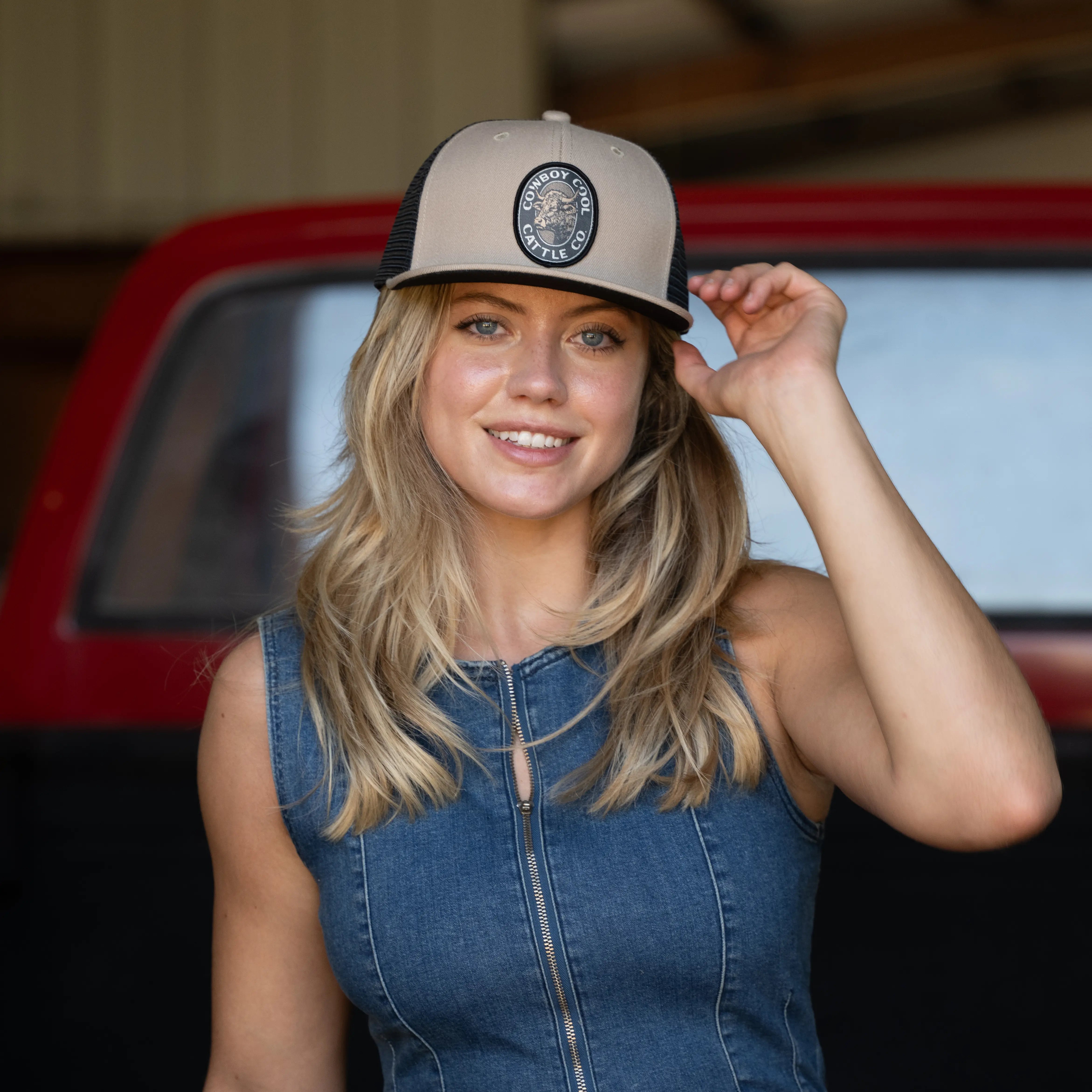 Woman wearing a western cap with a Cowboy Cool Cattle Company logo, standing in front of a red truck.