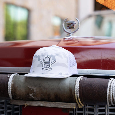 White camo trucker hat with cowboy hat logo, styled on vintage red car bumper