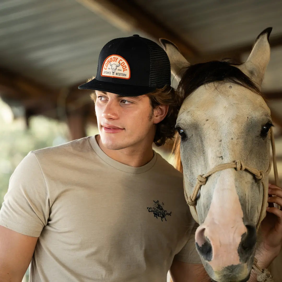 Cowboy with horse wearing Cowboy Cool Badlands Hat in black with bison skull patch and Untamed Western branding