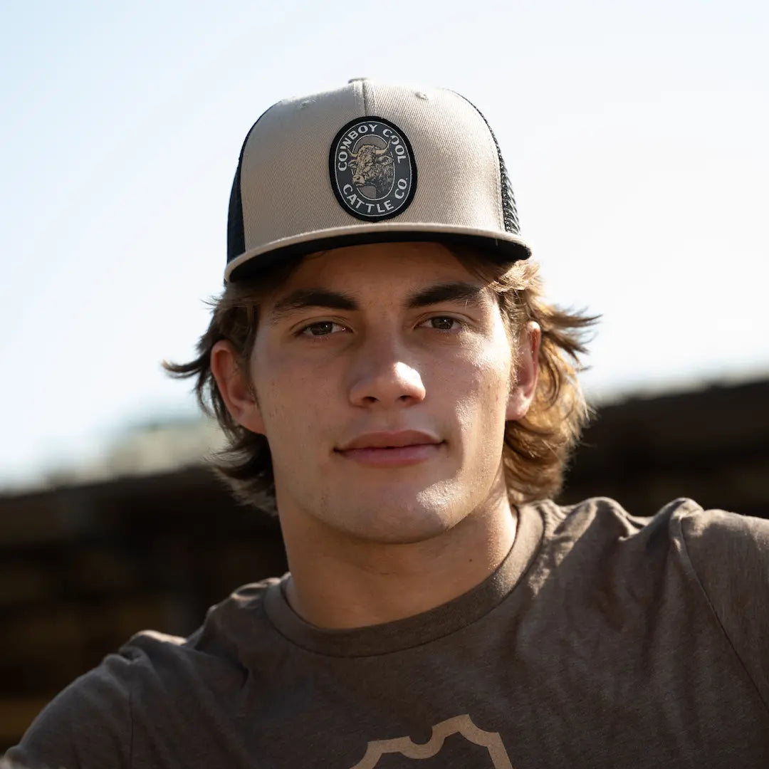 Man wearing a cowboy cool western cap with a Cattle Company logo against a blurred outdoor background