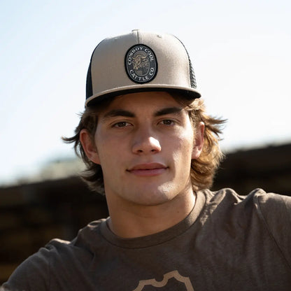 Man wearing a cowboy cool western cap with a Cattle Company logo against a blurred outdoor background