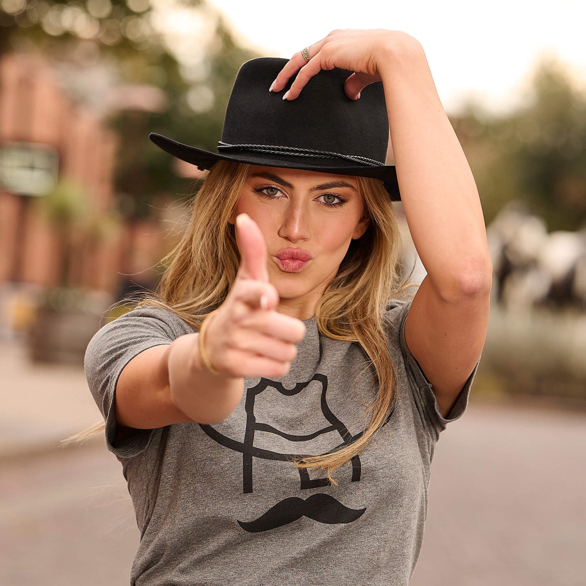 Female model wearing a Cowboy Cool Hank T-Shirt pointing at the camera.