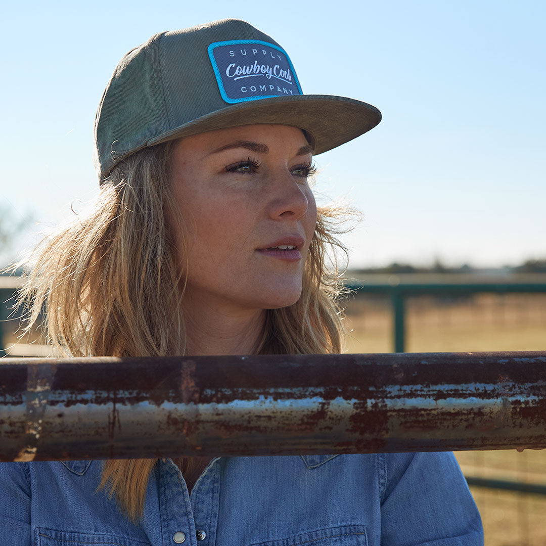 A woman looking off into the distance wearing a Cowboy Cool Houlihan Hat in Olive. 